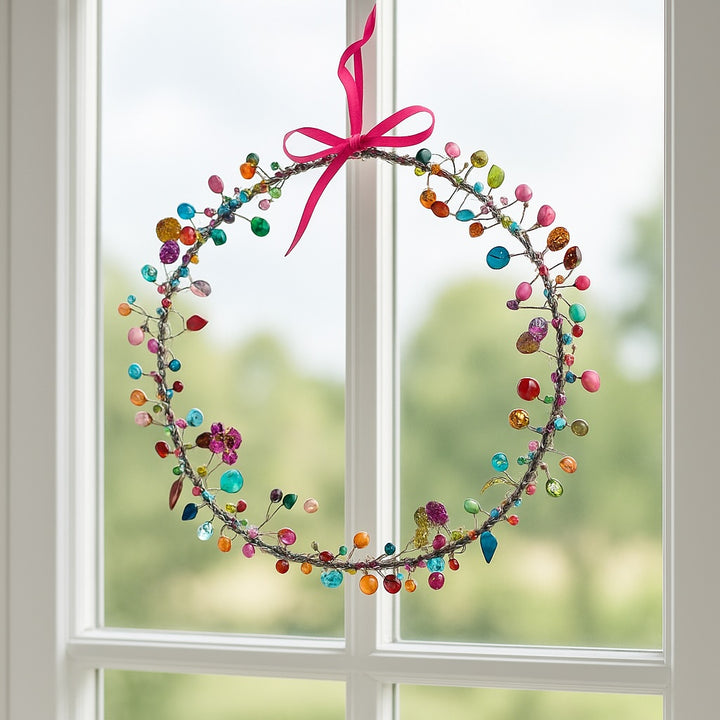 Decorative wreath with colorful beads and a pink ribbon hanging on a window.