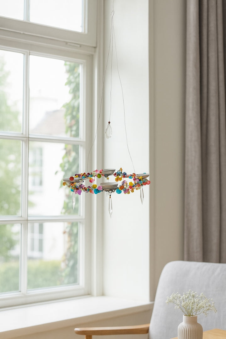 Modern chandelier with colourful beads in a room with a large window and grey curtains.