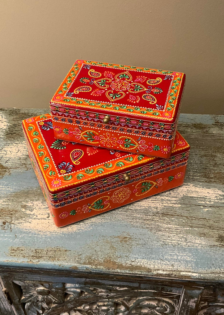 Two ornate red and orange boxes with intricate patterns on a wooden surface.