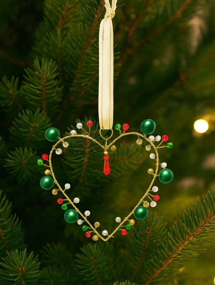 Heart-shaped Christmas ornament with beads on a green tree