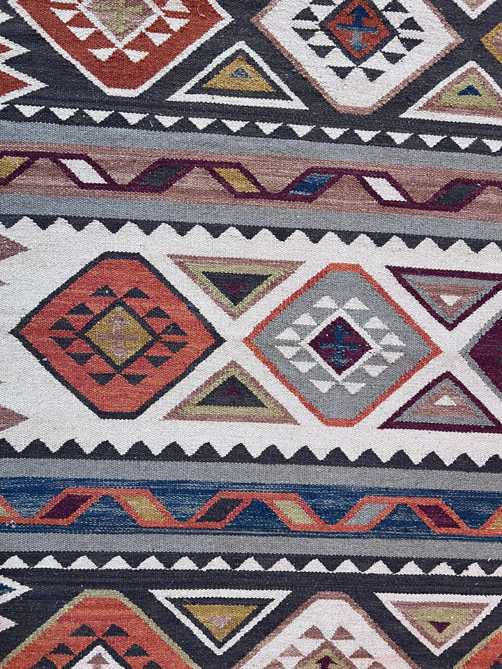 A close-up of a woven geometric rug with Southwestern-style patterns in rust red, navy, gray, cream, and olive green.