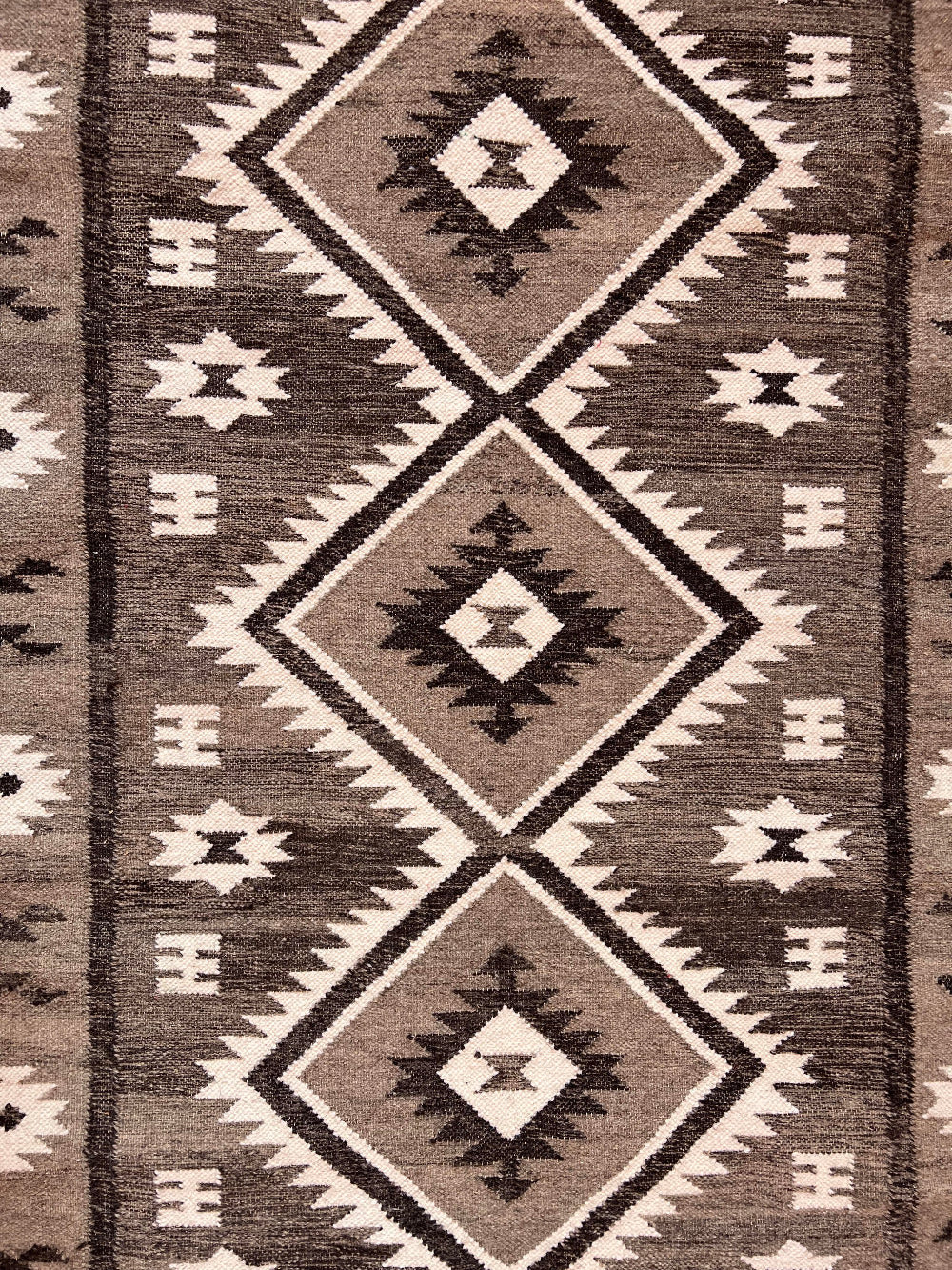 A close-up of a woven rug with a Southwestern geometric pattern in brown, grey and cream.