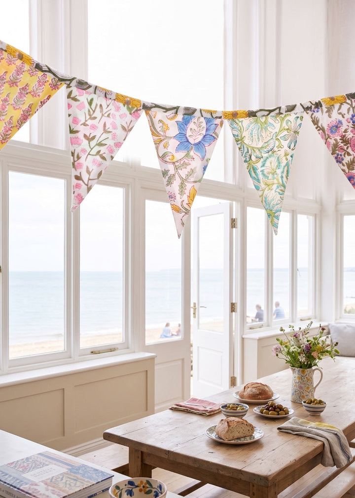 Sunlit room with floral bunting, wooden table, and books by a large window.