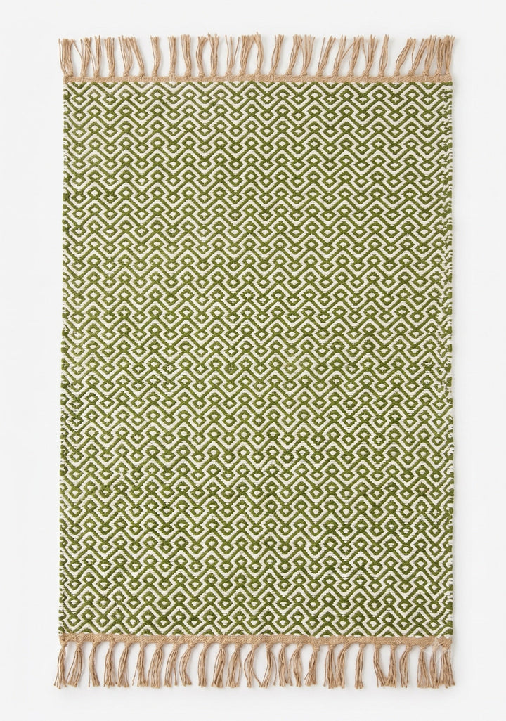 A rectangular woven rug with a repeating geometric pattern in olive green and cream, finished with natural beige fringed tassels on the top and bottom edges, shown flat against a light off-white background.