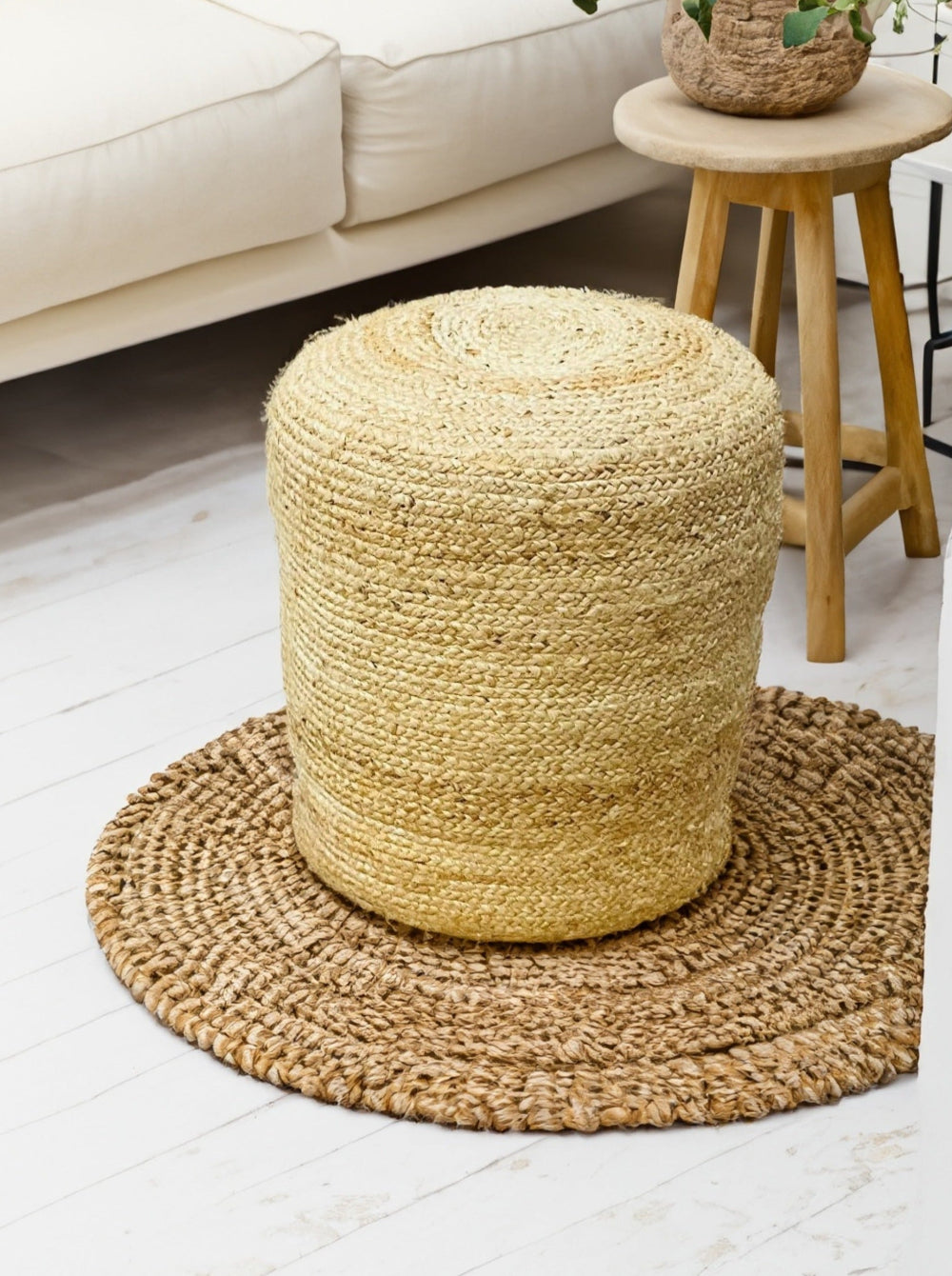 Handmade tall round jute pouffe on woven rug in living room setting