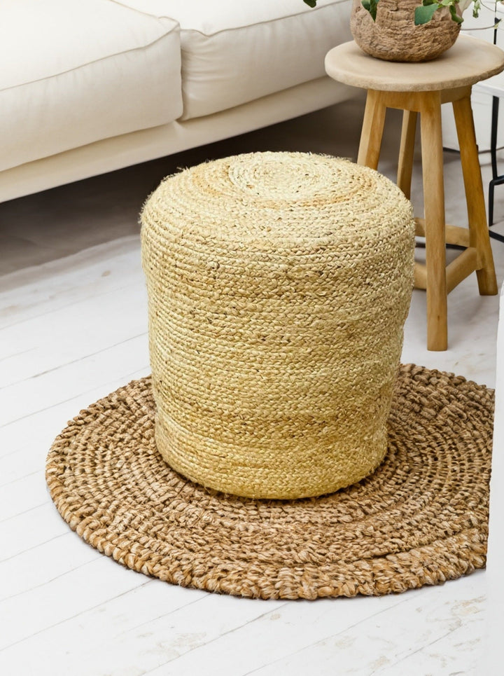 Handmade tall round jute pouffe on woven rug in living room setting