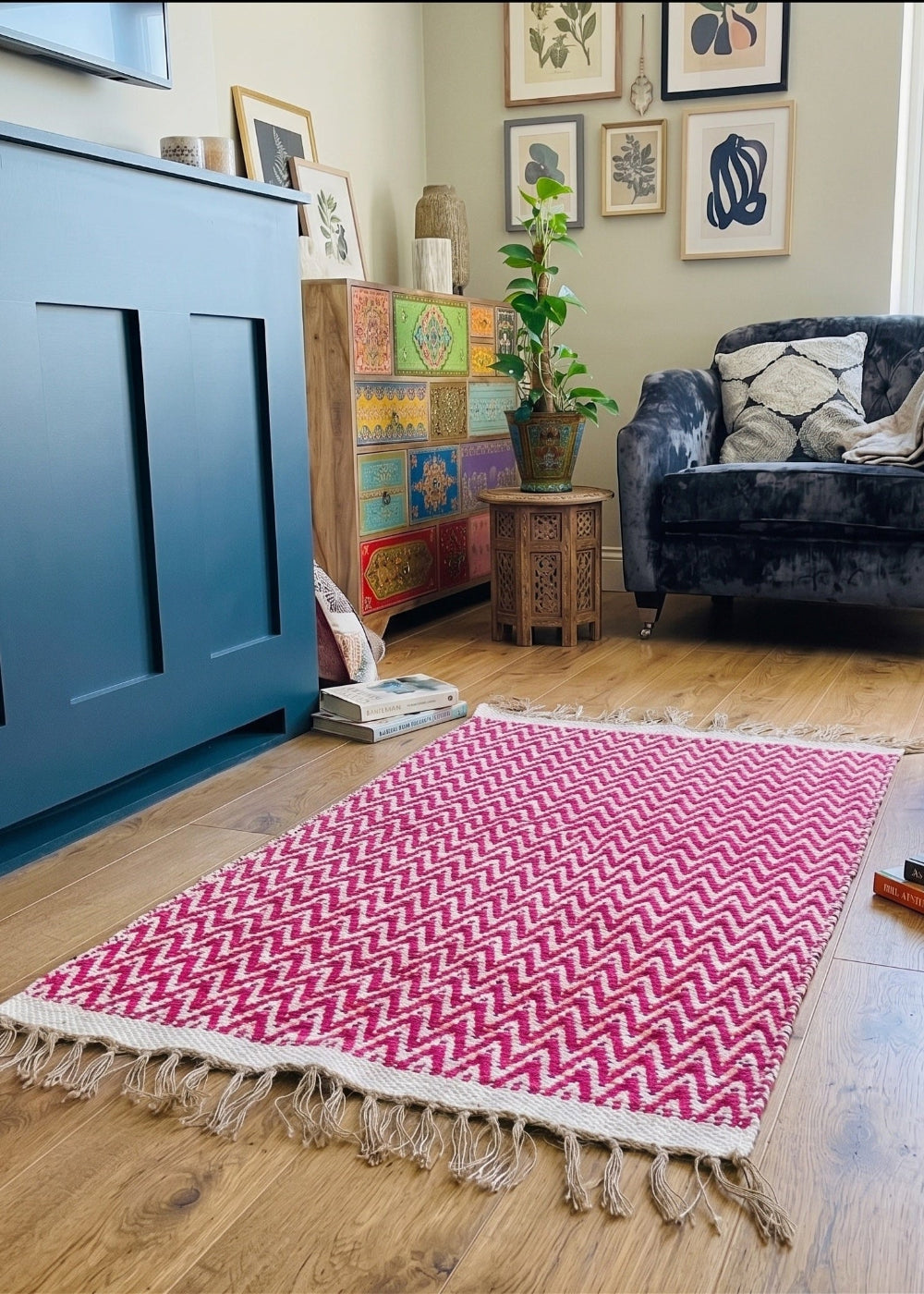 Living room with a pink and white patterned rug, blue cabinet, and colourful armchair.
