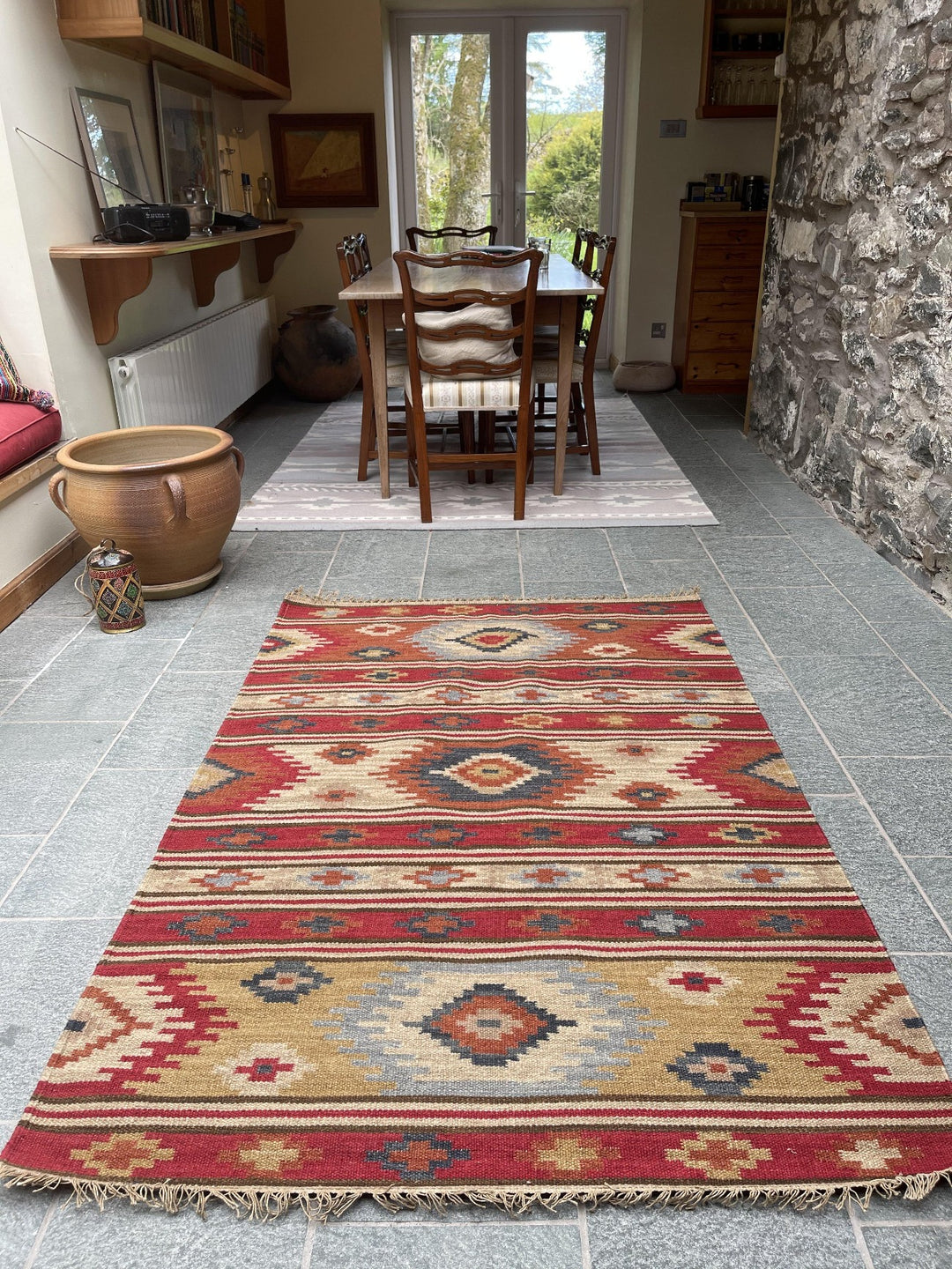 Kilim wool area rug on stone floor in a dining area with wooden table and chairs